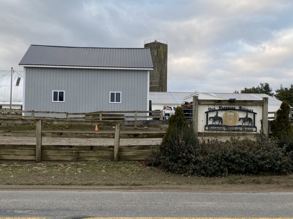 Grey Barn With Sign that says "Our Pleasure Stables" in front of barn.